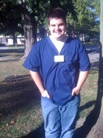 Konner Garnett stands outside his home in Halstead, wearing his work shirt and name tag.