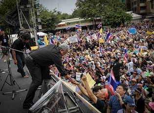 สุเทพ เทือกสุบรรณ ทักทายผู้สนับสนุนบนเวทีโค่นล้มระบอบทักษิณ  ที่อนุสาวรีย์ประชาธิปไตย ถ.ราชดำเนิน ที่มาของภาพ เพจสุเทพ เทือกสุบรรณ