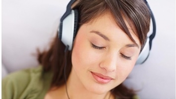 หญิงสาวกำลังนอนฟังเพลงจากหูฟังแบบครอบหู