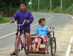 นายสมพงษ์ ปั่นจักยานพ่วงข้างโดยมีน้องเมย์ หลานสาวที่สมองพิการไปด้วย