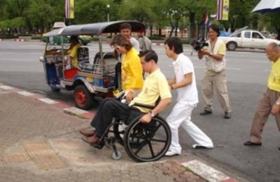 ผู้ดูแลคนพิการช่วยเข็นรถเข็นคนพิการขึ้นทางลาด