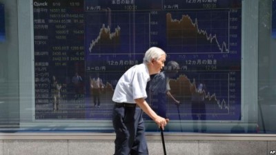 FILE - An elderly man walks by an electronic stock board of a securities firm in Tokyo, Aug. 19, 2016. The elderly are said to be more prone to depression as they became more isolated from their communities.